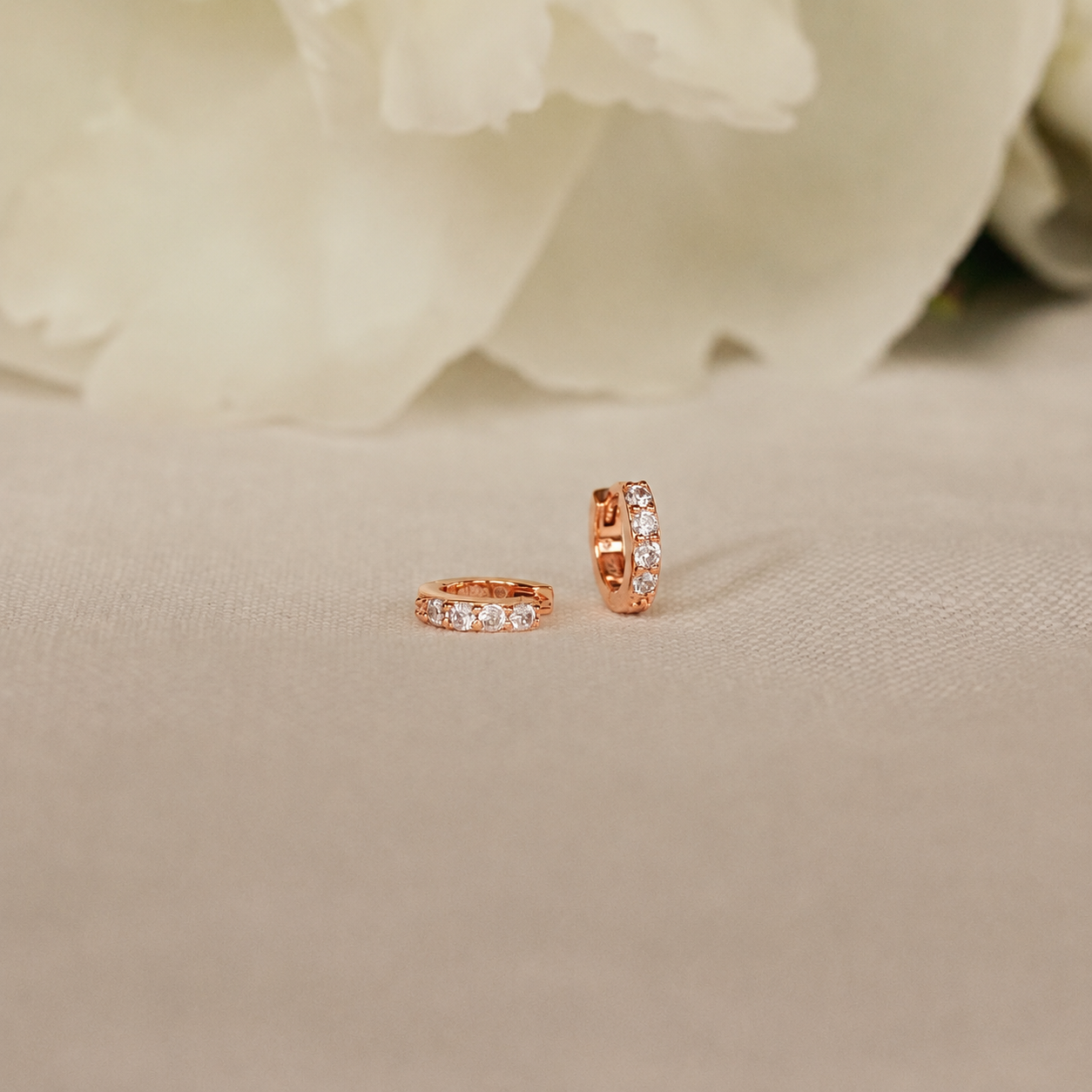 Rose gold hoop earrings with embedded diamonds on a beige fabric background.